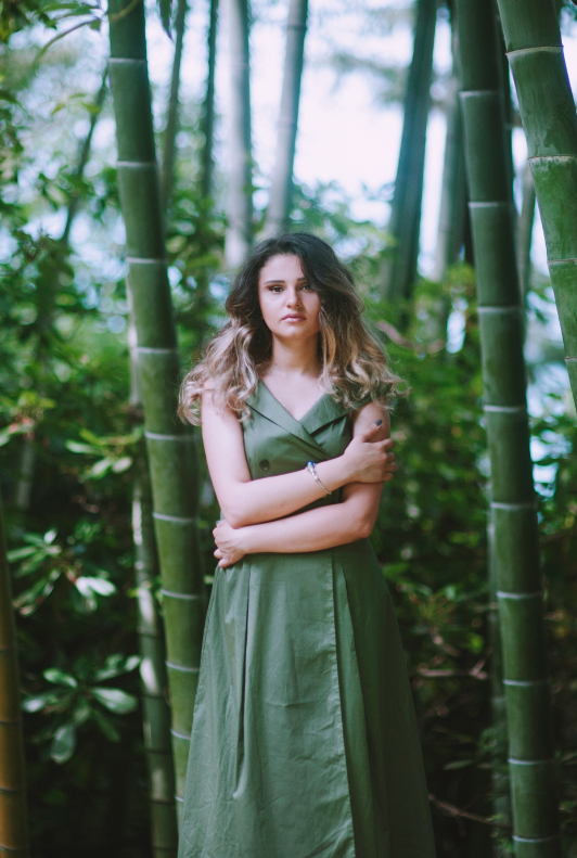 Vacker kvinna med en grön klänning stående framför en bakgrund av bambuträd