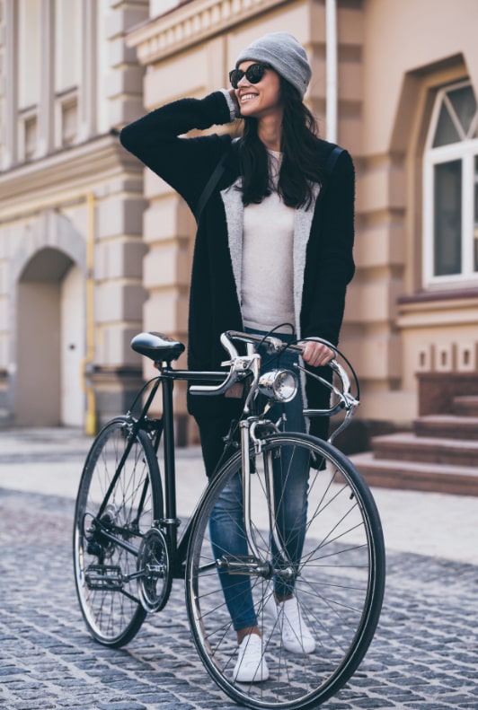 Kvinna stående på kullersten i stan samtidigt som hon håller en klassisk svart cykel med ena handen