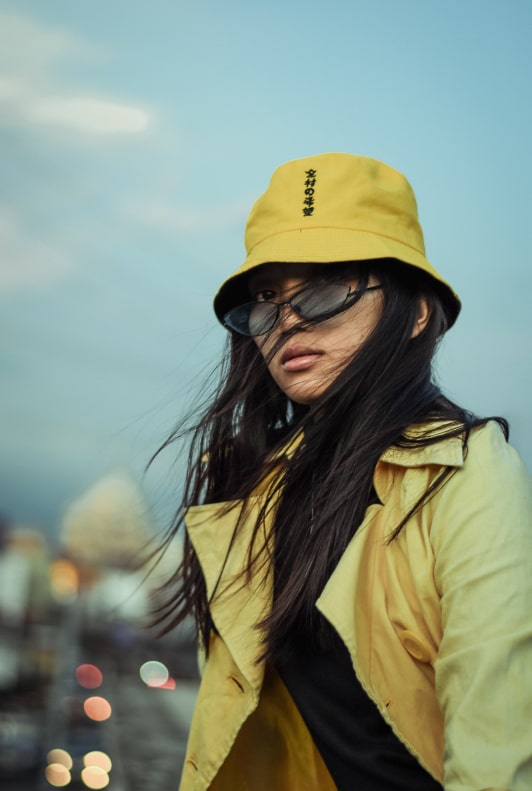Vacker kvinna med en gul bucket-hatt, solglasögon och gul jacka