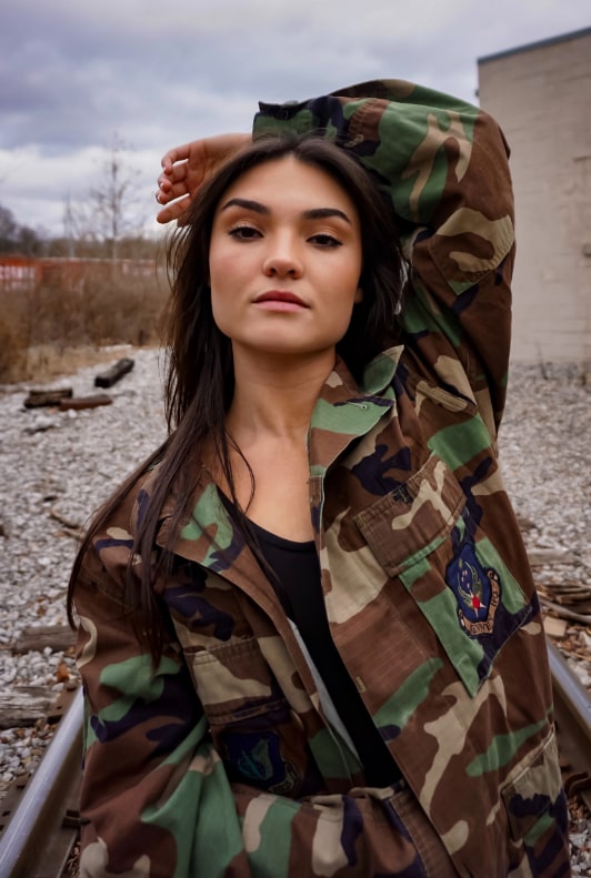 Vacker brunhårig kvinna med ena handen bakom huvudet bärande en militärinspirerad jacka