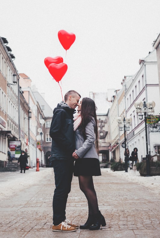 Ett par som kysser varandra med tre hjärtformade ballonger i bakgrunden