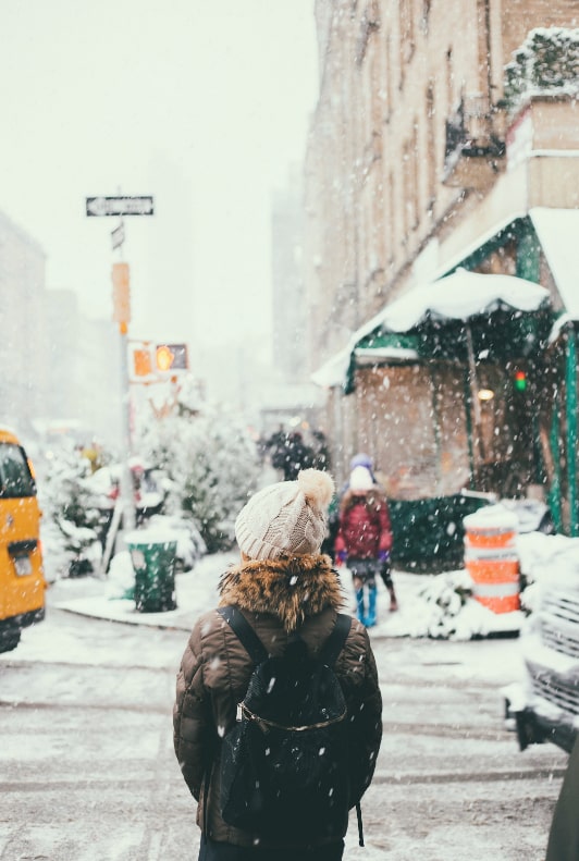 Kvinna med toppluva och jacka i stan under snöfall