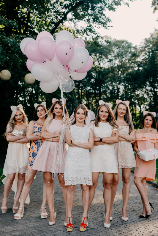 7 kvinnor med olika bröllopsklänningar var den främsta kvinnan står med en bukett rosa balonger i handen