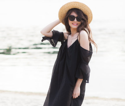 Kvinna i svart strandklänning, solglasögon och stråhatt