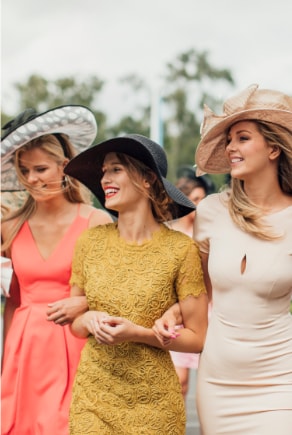 Tre eleganta kvinnor i hatt och klänning i ett festligt sammanhang